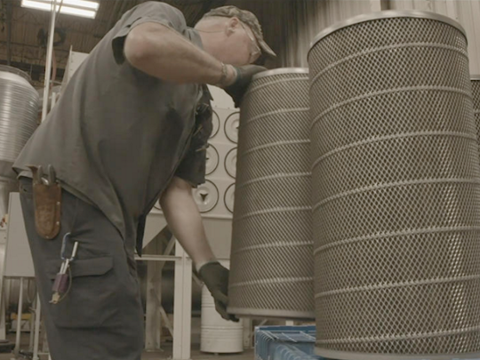 An operator lifting a dust collector cartridge filter.